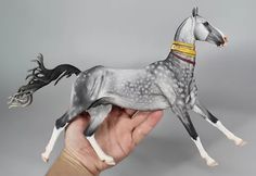 a hand holding a gray and white toy horse in it's right hand on a grey background