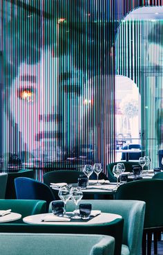 the interior of a restaurant with green and blue chairs, round tables and striped walls