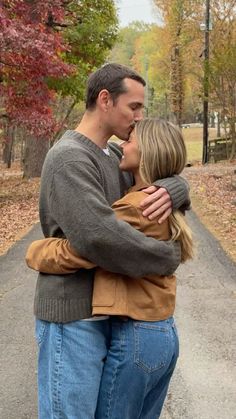 a man and woman hugging each other in the middle of a road surrounded by trees