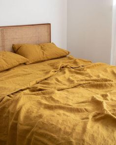 an unmade bed with yellow linens in a white walled room next to a window