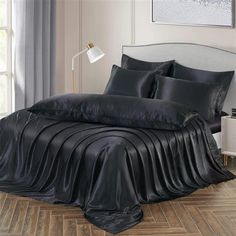 a bed with black sheets and pillows on top of wooden flooring next to a window