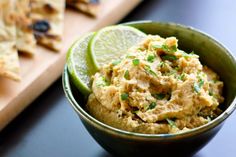 a bowl filled with hummus next to tortilla chips on a cutting board