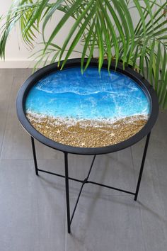 a round table with a blue and white ocean scene on the top, sitting next to a palm tree