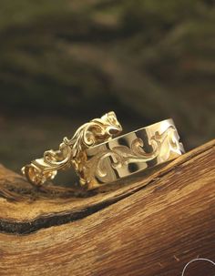 two gold wedding bands sitting on top of a wooden piece