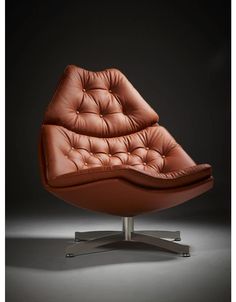 an orange leather chair sitting on top of a metal base with a black wall in the background