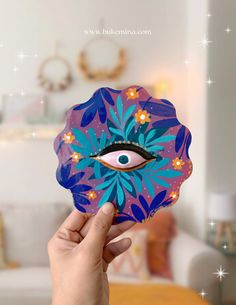 a hand holding up a purple and blue eyeball with flowers on it in front of a bed