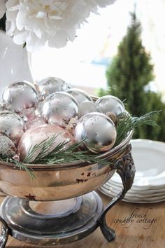 a bowl filled with ornaments on top of a wooden table next to plates and flowers