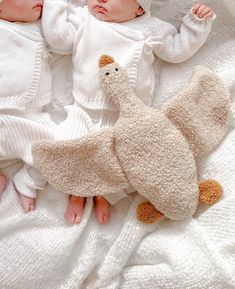 two baby babies laying next to each other on a white blanket with a stuffed animal