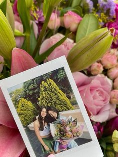 a person holding up a polaroid photo with flowers in the back ground behind them