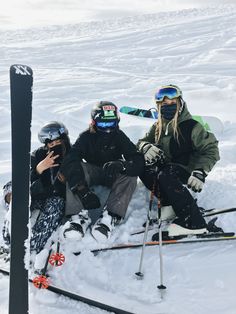 three people sitting on the snow with skis and poles in their hands, posing for a photo