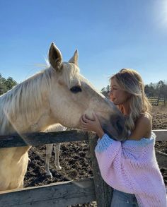 a woman standing next to a white horse in a pen with her hand on the nose