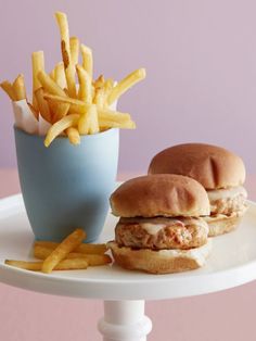 a chicken sandwich and french fries on a white plate with a blue cup in the background