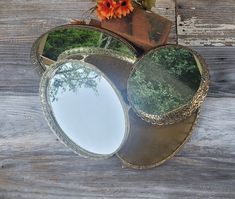 a mirror sitting on top of a wooden table next to a vase with an orange flower