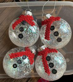 three glass ornaments with buttons and red ribbon on them sitting in a plastic container next to a christmas tree ornament