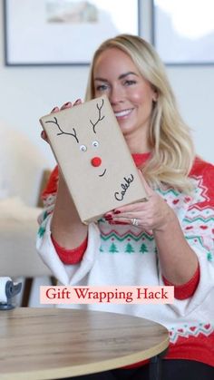 a woman holding up a gift wrapped in brown paper with a reindeer face on it