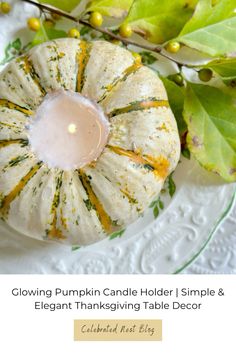 a white pumpkin sitting on top of a table next to green leaves and a candle