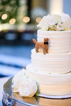 a wedding cake with white flowers and a small dog figurine on the top