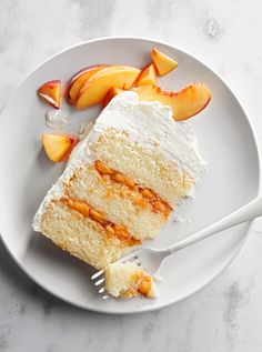 a piece of cake with white frosting and peach slices on a plate next to a fork