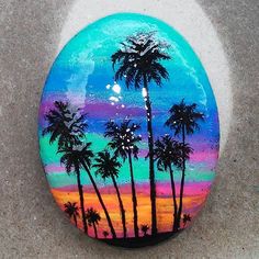 a painted rock with palm trees and sunset in the background, on a concrete surface