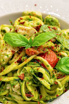 a white bowl filled with zucchini noodles and pesto garnishes