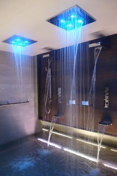 two shower heads are connected to the wall with blue lights on them and water running from them