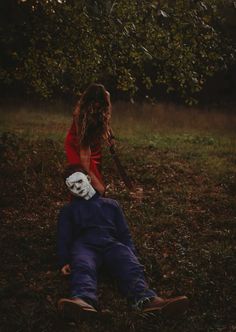 a person laying in the grass with a mask on their face and another person holding a baseball bat