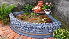 a fish pond in the middle of a brick patio with flowers and plants around it