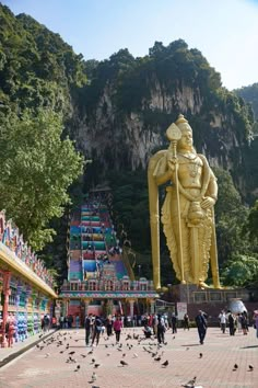 a large golden statue sitting in the middle of a park next to a mountain covered with trees