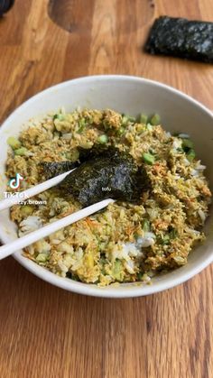 a bowl filled with rice and vegetables on top of a wooden table next to chopsticks