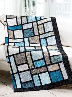 a white couch with a blue and black quilt on it's back next to a window