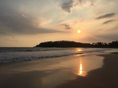 the sun is setting over an island in the ocean with waves lapping on it