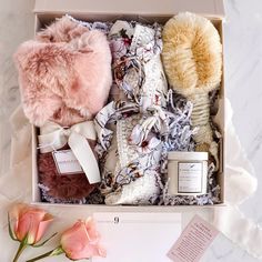 an open box filled with clothing and flowers on top of a white table cloth next to a pink rose