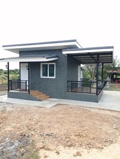 a small gray house sitting on top of a dirt field next to a building with stairs leading up to it