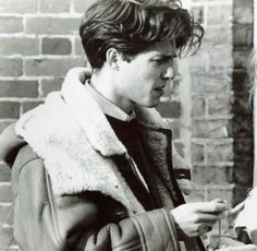 black and white photograph of a woman looking at her cell phone while standing in front of a brick wall