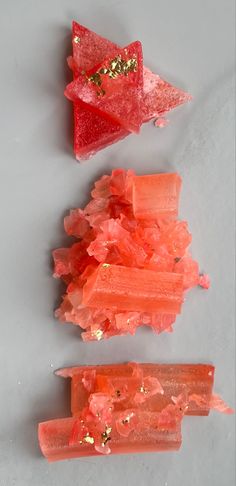 three pieces of red rock candy on a gray surface with gold flecks around them