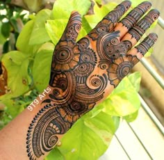 a woman's hand with henna tattoos on it and green leaves in the background