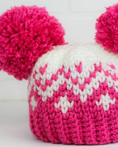 a pink and white knitted hat with pom - poms