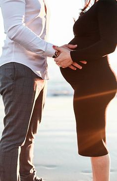 a pregnant woman standing next to a man holding her belly while the sun shines down