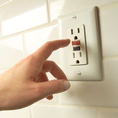 a person turning on an electrical outlet in a white tiled wall with their hand pointing at it