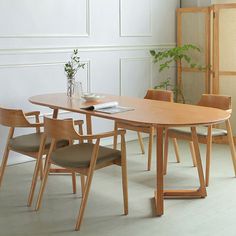 a wooden table with chairs around it in a white room next to a plant and bookshelf