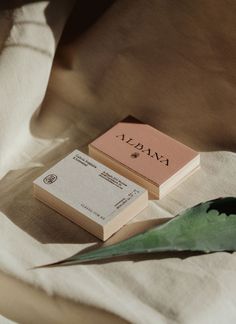 two business cards sitting on top of a table next to a green plant and white linen