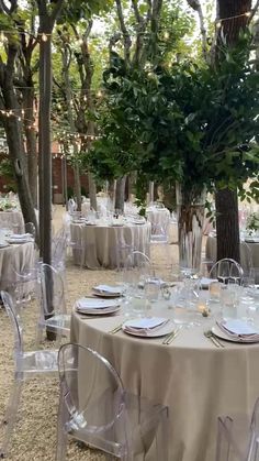 an outdoor dining area with clear chairs and round tables set up for formal function, surrounded by trees