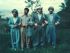 three men standing next to each other in front of a tree on a hill side