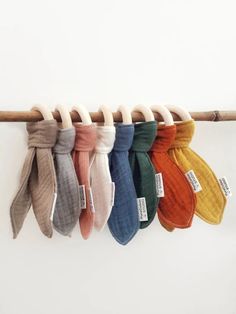 five different colors of ties hanging from a clothes line on a white wall with a wooden stick in the foreground