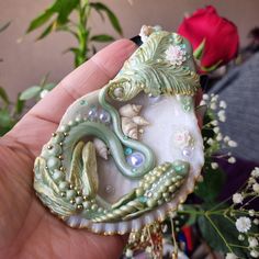 a close up of a person holding a small brooch with flowers in the background