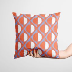 a person holding a pillow with an orange and blue design on it, in front of a white background