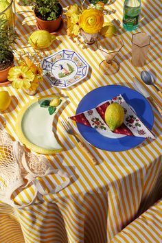 a table topped with plates covered in food next to lemons and flowers on top of a yellow striped table cloth