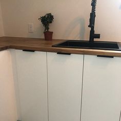 a kitchen with white cupboards and a black sink in the corner next to a potted plant