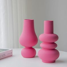 two pink vases sitting on top of a table next to a book and window