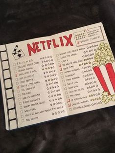 an open book with a movie list on it and a cup of popcorn next to it